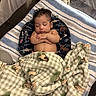 baby, infant, sleeping, child, face, curly_hair, closed_eyes, peaceful, blanket, playpen, cushion, portrait, indoors, cozy, bedding, patterned_blanket, resting, arms_crossed, nap, photograph