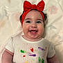baby, child, smiling, red_bow, headband, paint_splatter, white_shirt, happy, face, arm, skin, indoors, closeup, person, infant, cute, cheerful, expression, colorful, playful
