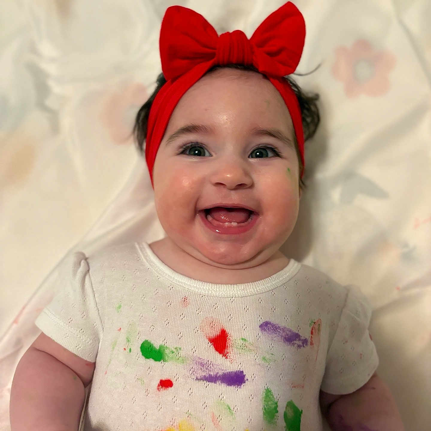 Salmah Pérez Acosta joined the competition — help win amazing prizes! arm, baby, cheerful, child, closeup, colorful, cute, expression, face, happy, headband, indoors, infant, paint_splatter, person, playful, red_bow, skin, smiling, white_shirt