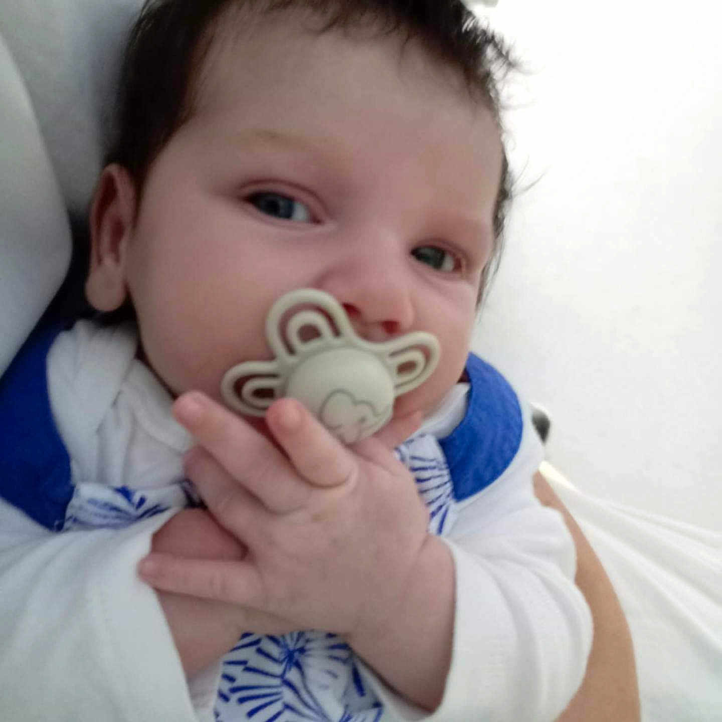 Emmy participe au concours pour gagner de l'argent avec cette photo : adult_arm, baby, blue_clothing, child, closeup, clothing_pattern, cute, expression, face, hand, holding, human, indoors, infant, newborn, pacifier, person, portrait, skin, white_clothing