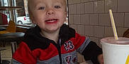 Liam is registered to the contest to win money with this photo: toddler, child, smile, indoor, restaurant, table, drink, cup, window, jacket, red, black, gray, face, hand, chair, tile_wall, autumn, tree, fast_food