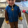 child, costume, police_uniform, smiling, indoor, living_room, couch, pillow, table, wooden_floor, shoes, person, happy, flooring, carpet, toy, casual, playful, young_child, face