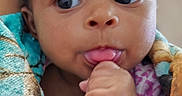 Zoey joined the competition — help win amazing prizes! baby, blanket, blue_eyes, child, close_up, colorful, curious, cute, eyes, face, fist, hand, indoor, infant, photography, pink_clothing, portrait, sitting, sucking_fingers, wrapped
