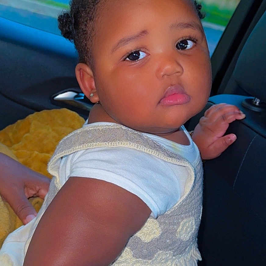 Salimatou Bah joined the competition — help win amazing prizes! baby, bantu_knots, blanket, car, child, curious, cute, face, greenery, hairstyle, hand, indoors, park, person, portrait, seat, skin, trees, white_clothing, window