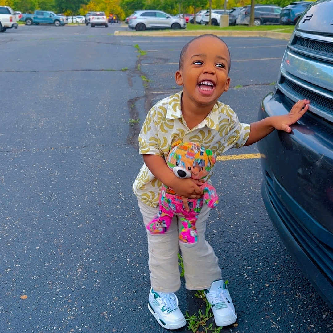 Saidou Bah joined the competition — help win amazing prizes! asphalt, car, casual_wear, child, clothing, daytime, greenery, happy, laughing, nature, outdoor, parking_lot, person, smiling, sneakers, teddy_bear, toddler, toy, trees, vehicle