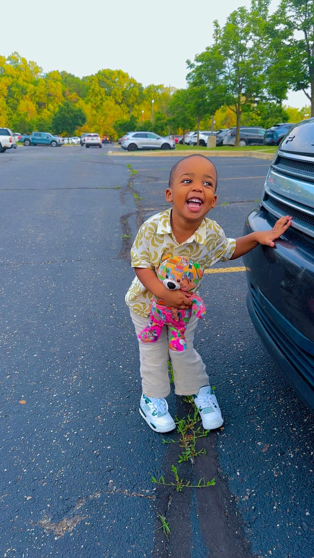 Saidou Bah joined the competition — help win amazing prizes! child, toddler, teddy_bear, parking_lot, car, asphalt, trees, greenery, sneakers, laughing, outdoor, toy, clothing, nature, daytime, person, smiling, casual_wear, vehicle, happy