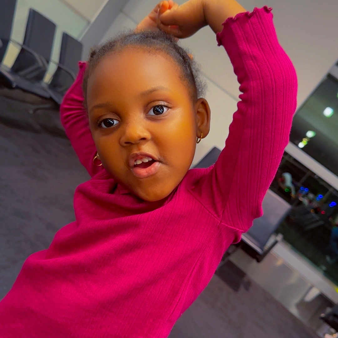 Fatimatou Bah joined the competition — help win amazing prizes! blue_pants, carpet, casual, chairs, child, cute, earrings, expression, girl, indoor, lighting, modern, person, pink_sweater, playful, pose, television, waiting_room, window, young