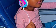 Fatimatou Bah is registered to the contest to win money with this photo: child, headphones, pink_bow, airplane_seat, window, music, relaxed, blue_seat, seatbelt, clothing, person, listening, seat, young, portrait, travel, cute, fun, happy, indoor