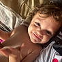 arm, bed, candid, child, closeup, curly_hair, expression, face, happy, indoors, light, person, pillow, red_heart, relaxing, shadow, shirt, skin, smiling, toddler