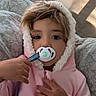 toddler, child, pacifier, pink_hoodie, cute, indoors, portrait, cozy, blanket, soft_lighting, curtains, hand, face, expression, young_child, baby, warm, comfort, cushion, sleepy