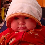 Josephine joined the competition — help win amazing prizes! baby, infant, child, hat, red_clothing, gingerbread_pattern, drool, face, indoor, wooden_cabinet, cute, chubby_cheeks, portrait, cozy, warm_lighting, curious_expression, sitting, clothing, headwear, room