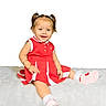 child, toddler, girl, smiling, portrait, red_dress, pink_shoes, pigtails, sitting, blanket, white_background, indoors, baby, happy, face, clothing, footwear, studio_photo, bracelet, playful