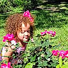child, curly_hair, cute, flowers, garden, girl, greenery, happy, leaves, nature, outdoor, pink, pink_bow, plants, portrait, roses, smelling, summer, sunlight, young