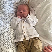 Elio participe au concours pour gagner de l'argent avec cette photo : baby, newborn, infant, bed, pillow, blanket, bedding, chevron_pattern, white_shirt, khaki_pants, socks, button_down_shirt, lying_down, cute, portrait, hand, adult_hand, indoor, cozy, soft_light
