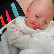 Oaklynn joined the competition — help win amazing prizes! baby, blanket, child, close_up, clothing, colorful, cozy, cute, face, happy, indoor, infant, photograph, portrait, seated, smiling, soft, swaddle, tongue_out, white