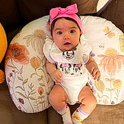 Anya is registered to the contest to win money with this photo: baby, bib, bow, brown, child, comfortable, couch, cute, floral_pillow, happy, headband, indoors, infant, minnie_mouse, person, pink, portrait, relaxed, smiling, socks