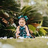 toddler, child, braids, bows, green_dress, grass, flowers, outdoor, nature, plants, leaves, sunlight, portrait, sitting, cute, curious, young_child, daylight, garden, peaceful