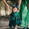 toddler, child, green_dress, holding_hands, adult, outdoor, walking, nature, pathway, bow, footwear, person, family, support, cute, happy, sunlight, shade, dress, young_child