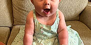 Addison is registered to the contest to win money with this photo: baby, child, girl, bow, headband, dress, floral, socks, couch, beige, furniture, indoors, cute, surprised, happy, smiling, sitting, person, portrait, infant