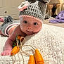Addison is registered to the contest to win money with this photo: baby, infant, crochet_hat, knitted_blanket, toy_carrots, indoor, bedroom, lamp, cute, child, person, soft_texture, portrait, lying_down, hand, blue_eyes, pink_skin, cozy, decor, warm_lighting