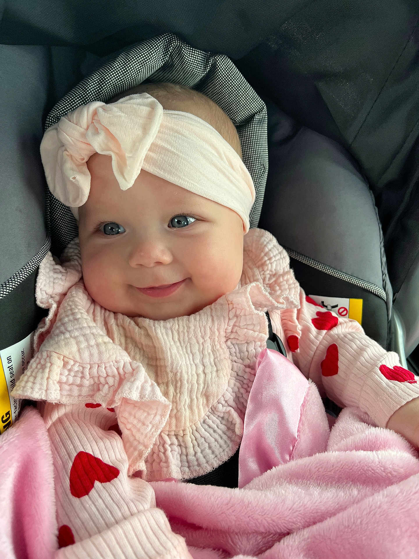 Addison is registered to the contest to win money with this photo: baby, infant, smile, headband, pink, heart_pattern, car_seat, blanket, cute, child, portrait, clothing, soft, happy, face, closeup, adorable, cozy, seat, young