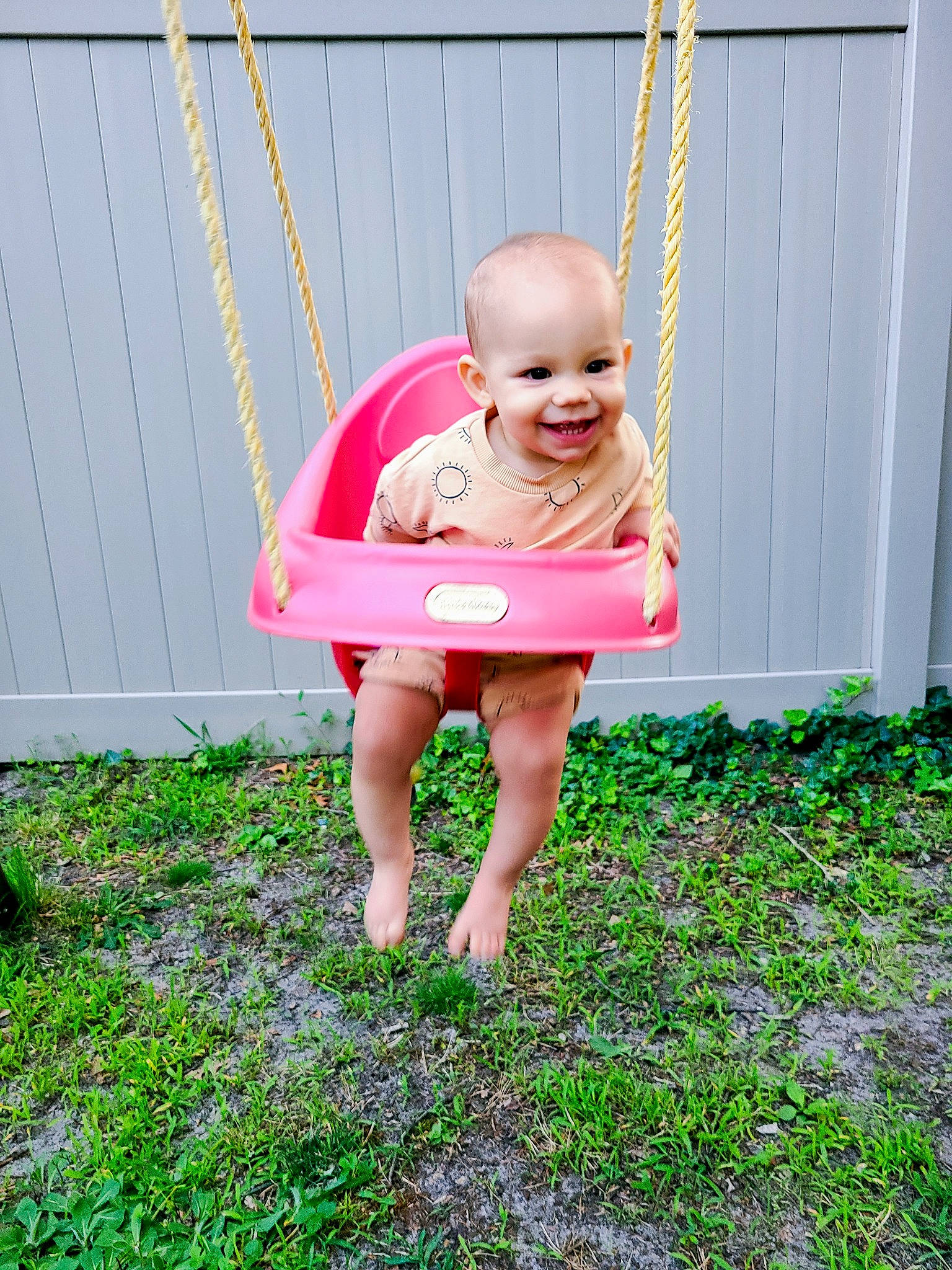 Freyja is registered to the contest to win money with this photo: baby, baby_toddler_clothing, child, fun, garden, grass, green, groundcover, happy, human_leg, joy, lawn, leisure, magenta, people_in_nature, person, plant, sitting, smile, swing