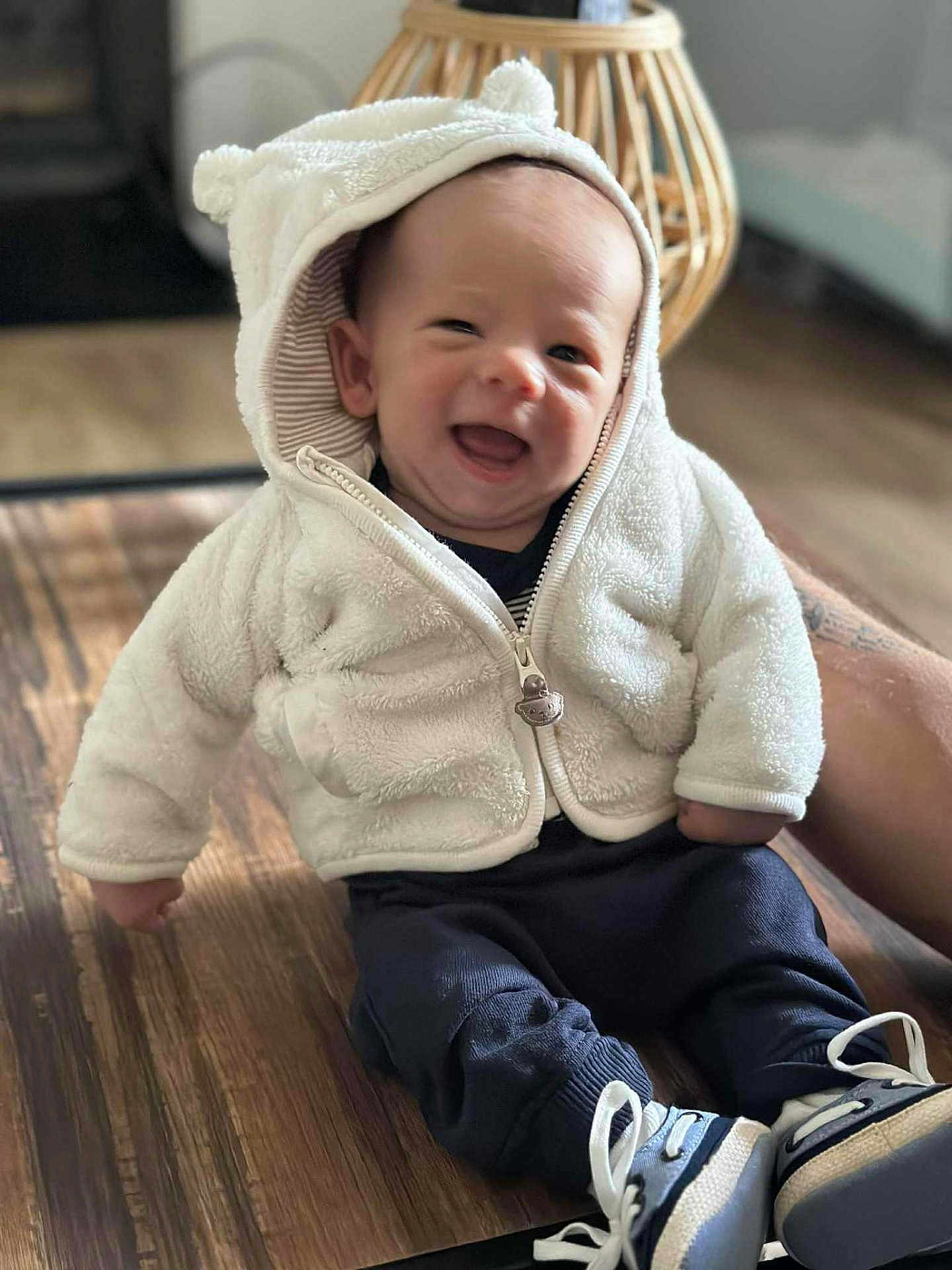 Tilio a rejoint le concours — aidez-le/la à gagner de superbes lots ! baby, child, smiling, hooded_jacket, white_jacket, bear_ears, sneakers, navy_pants, wooden_surface, indoor, happy, cute, infant, person, portrait, sitting, cozy, warm_clothing, hand, face