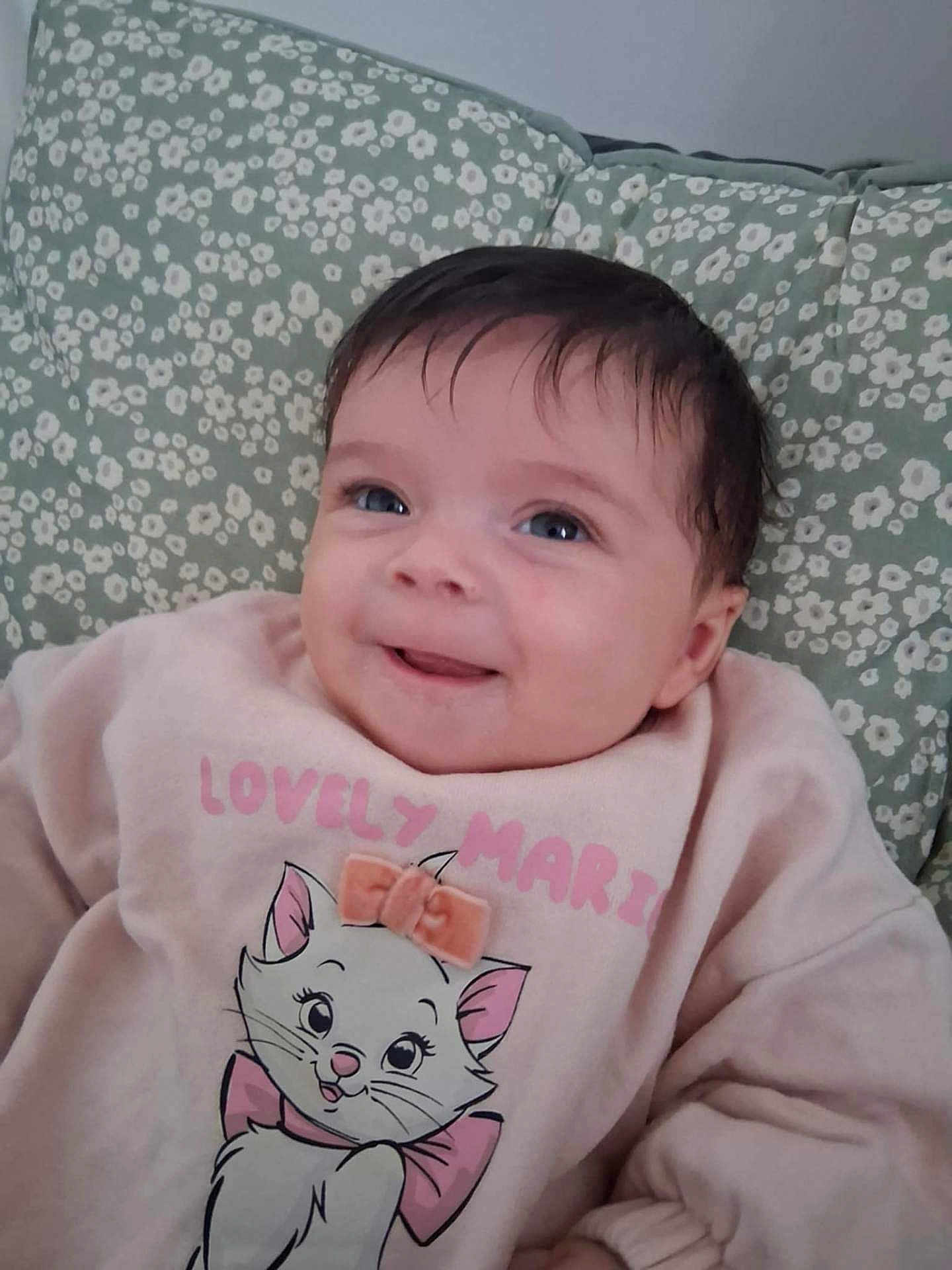 Aluney participe au concours pour gagner de l'argent avec cette photo : baby, smiling, face, child, sweatshirt, cartoon, cat, bow, cushion, pattern, floral, pink, clothing, indoors, cute, happy, portrait, skin, hair, infant