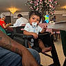 baby, casual_clothing, chair, child, curly_hair, cute, decor, dining_room, family, flower_tree, high_chair, indoor, pacifier, people, person, pink_flowers, portrait, restaurant, table, toddler