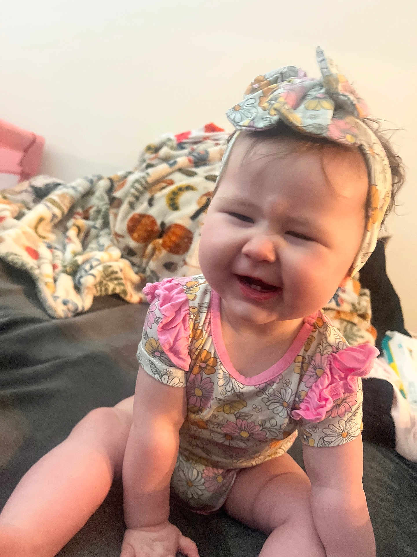 Scarlett is registered to the contest to win money with this photo: baby, child, infant, smiling, sitting, headband, floral_pattern, pink, cute, indoors, blanket, bed, cozy, person, face, cheeks, clothing, happy, young, expression
