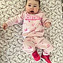baby, infant, child, pink_clothing, barbie, sneakers, patterned_sheet, bows, lying_down, cute, face, person, indoor, apparel, footwear, happy, young_child, casual_wear, portrait, baby_girl