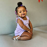 Claudia is registered to the contest to win money with this photo: toddler, child, smiling, sitting, purple_outfit, beads, hair, sandals, couch, indoor, cute, happy, girl, portrait, fashion, skin, face, young_child, comfort, seated