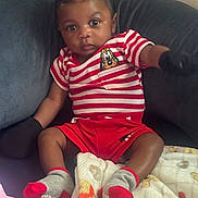 Armon is registered to the contest to win money with this photo: baby, black_gloves, blanket, casual, child, clothing, couch, curious, cute, gray_socks, home, indoor, infant, person, portrait, red_shorts, seated, soft_lighting, striped_shirt, young_child