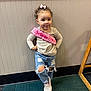birthday_princess, birthday_sash, bow, carpet, casual_clothing, cheeky_expression, child, curly_hair, hand_on_hip, indoor, long_sleeve, pose, ripped_jeans, smile, sneakers, standing, toddler, wall_paneling, wood_trim, young_girl