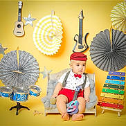 Ibrahim participe au concours pour gagner de l'argent avec cette photo : baby, child, toy_guitar, toy_microphone, xylophone, miniature_couch, musical_instruments, decorations, yellow_background, red_hat, red_bow_tie, red_shorts, white_shirt, polka_dots, stars, drum_set, colorful, indoor, portrait, cute