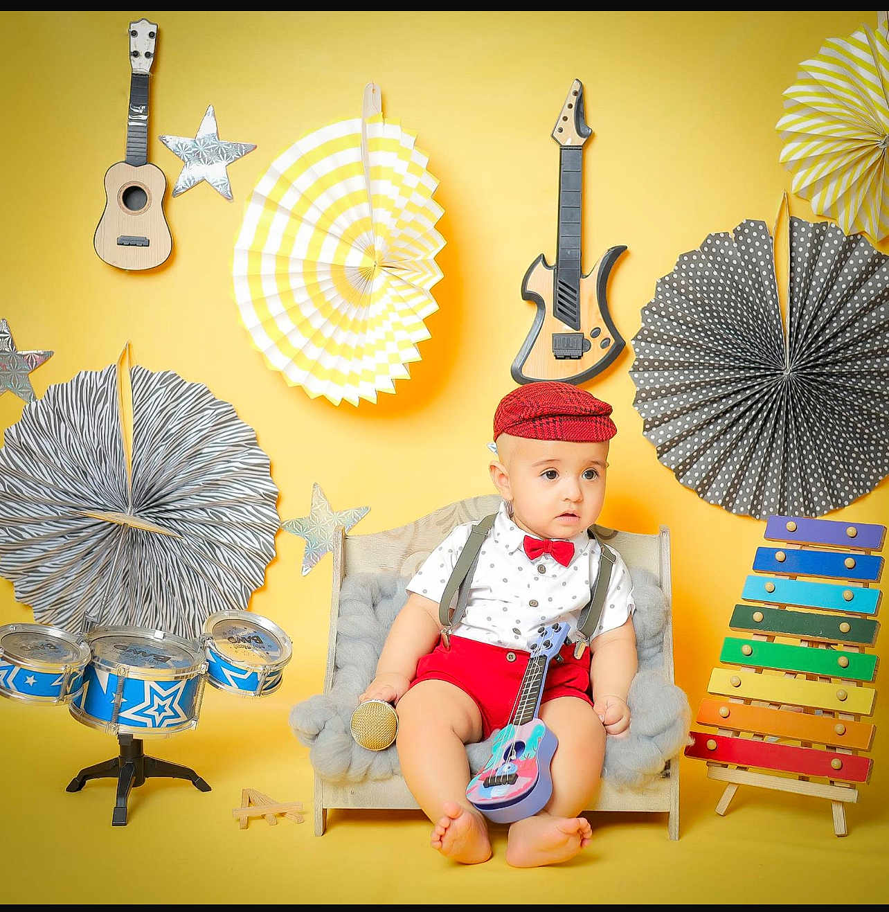 Ibrahim participe au concours pour gagner de l'argent avec cette photo : baby, child, toy_guitar, toy_microphone, xylophone, miniature_couch, musical_instruments, decorations, yellow_background, red_hat, red_bow_tie, red_shorts, white_shirt, polka_dots, stars, drum_set, colorful, indoor, portrait, cute