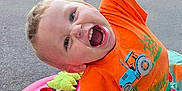 Junior is registered to the contest to win money with this photo: child, clothing, daylight, dogs, expression, face, greenery, happy, laughter, orange_shirt, outdoor, pavement, person, plastic, playful, playtime, shoes, toddler, toy, walker