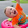 Junior is registered to the contest to win money with this photo: toddler, child, orange_shirt, walker, toy, outdoor, laughter, playful, happy, greenery, dogs, pavement, daylight, expression, face, person, clothing, shoes, plastic, playtime