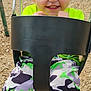 Junior is registered to the contest to win money with this photo: child, toddler, swing, playground, happy, smiling, outdoor, camouflage_pants, neon_shirt, wood_chips, fence, play_equipment, sneakers, fun, daylight, person, park, youth, casual_clothing, active