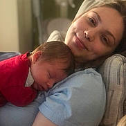 Sebastian is registered to the contest to win money with this photo: baby, woman, sleeping, smiling, indoor, closeup, face, person, child, love, cuddle, rest, comfort, red_clothing, blue_shirt, skin, head, hair, portrait, relaxation