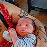 newborn, baby, sleeping, infant, portrait, close_up, face, hands, blanket, red_blanket, blue_clothing, adult_arms, tattoos, cuddling, indoors, wood_floor, playpen, graco, peaceful, family