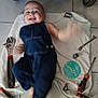arm_movement, baby, blue_clothing, child, denim_overalls, face, floor_tiles, hand_tools, happy, indoor, infant, lying_down, motion_blur, person, playful, screwdriver, smile, tools, towel, wrench