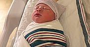 Samir is registered to the contest to win money with this photo: baby, bassinette, birth, blanket, cozy, cute, face, hat, head, hospital, hospital_room, infant, newborn, person, portrait, resting, sign, sleeping, striped, swaddled