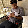 young_man, newborn, baby, hospital, couch, blanket, hat, indoor, person, holding, love, bonding, chain_necklace, bracelet, curly_hair, medical_equipment, cup, comfort, tenderness, casual_clothing