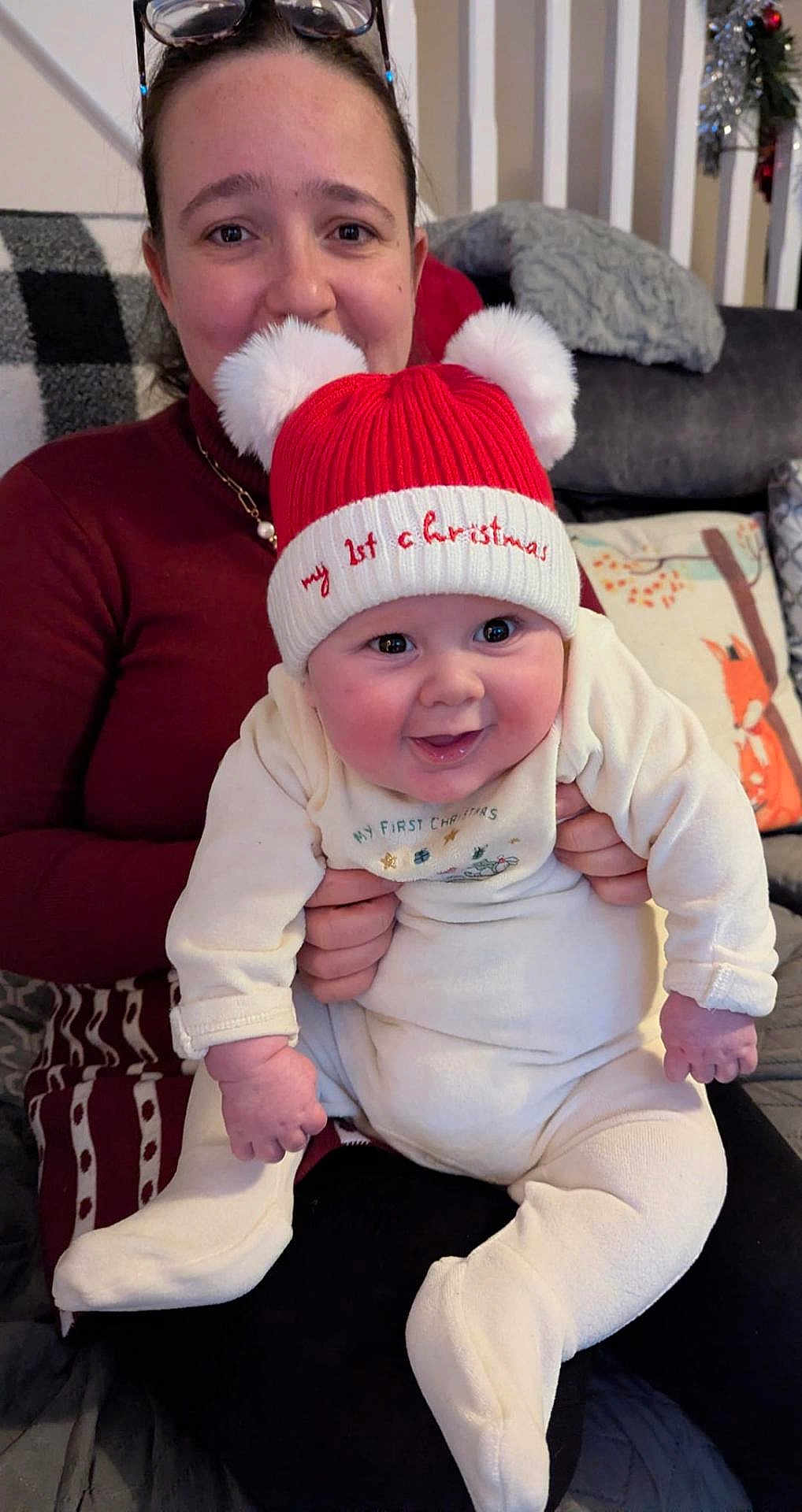 Raphael is registered to the contest to win money with this photo: baby, child, adult, smile, hat, red_hat, christmas, holiday, indoor, couch, blanket, pillow, woman, holding, cute, warm_clothing, festive, happy, face, portrait