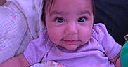 Braylee joined the competition — help win amazing prizes! baby, child, infant, portrait, face, smiling, blanket, purple_clothing, cute, indoors, cushion, hair_ponytail, cozy, soft_toys, closeup, happy, person, baby_girl, comfort, resting