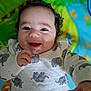 baby, smiling, infant, child, curly_hair, elephant_print, white_clothing, play_mat, colorful_background, happy, face, hand, cute, portrait, indoors, young_child, cozy, lying_down, closeup, cheerful