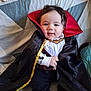 baby, bed, black, blanket, cape, child, clothing, costume, cute, face, hair, indoor, lying_down, pattern, person, red, smile, sock, vampire, white