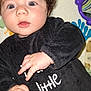 baby, child, face, blue_eyes, curly_hair, black_clothing, hand, infant, portrait, cute, indoor, toy, striped_cushion, playmat, expression, person, closeup, young_child, mustache_graphic, curiosity