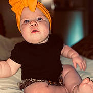 Oakley joined the competition — help win amazing prizes! baby, child, headwrap, orange, bow, black_shirt, shorts, barefoot, sitting, curious, indoor, soft_lighting, chubby, wide_eyes, cute, infant, pale_skin, portrait, closeup, bed